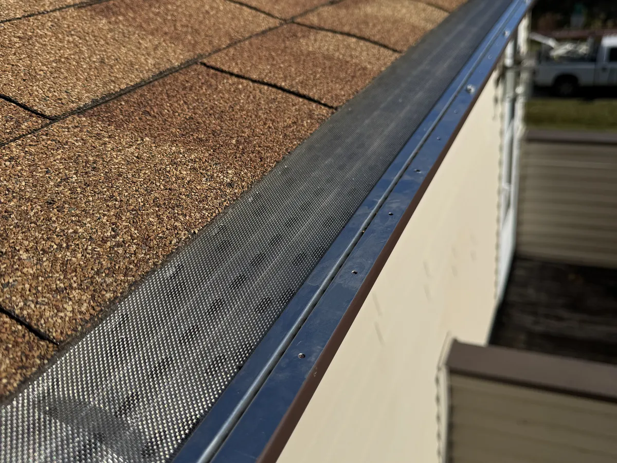 Close-up of a black micro-mesh gutter guard installed along a shingle roof