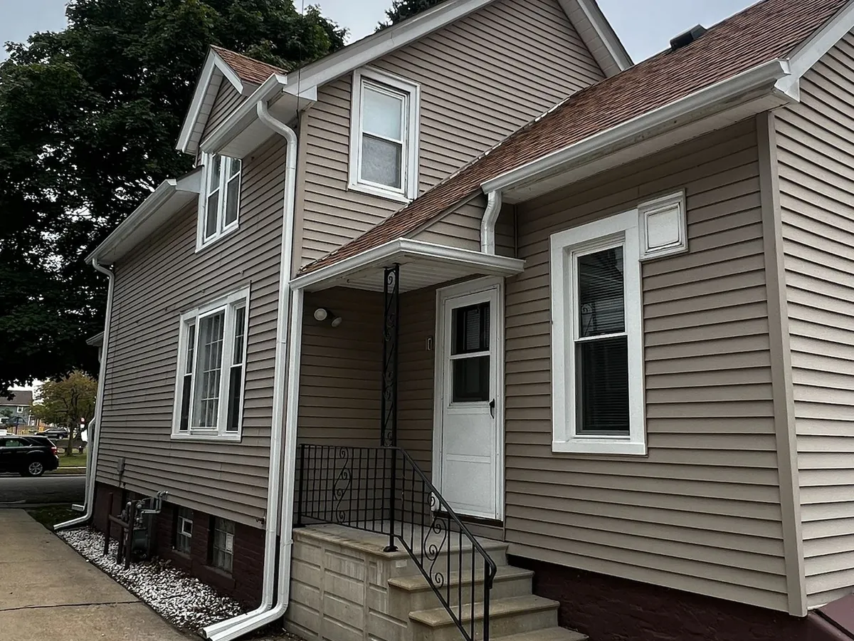 White downspout installed beside the front entry of a tan home