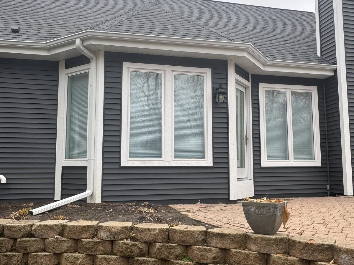 White seamless gutters installed on a gray home with a bay window