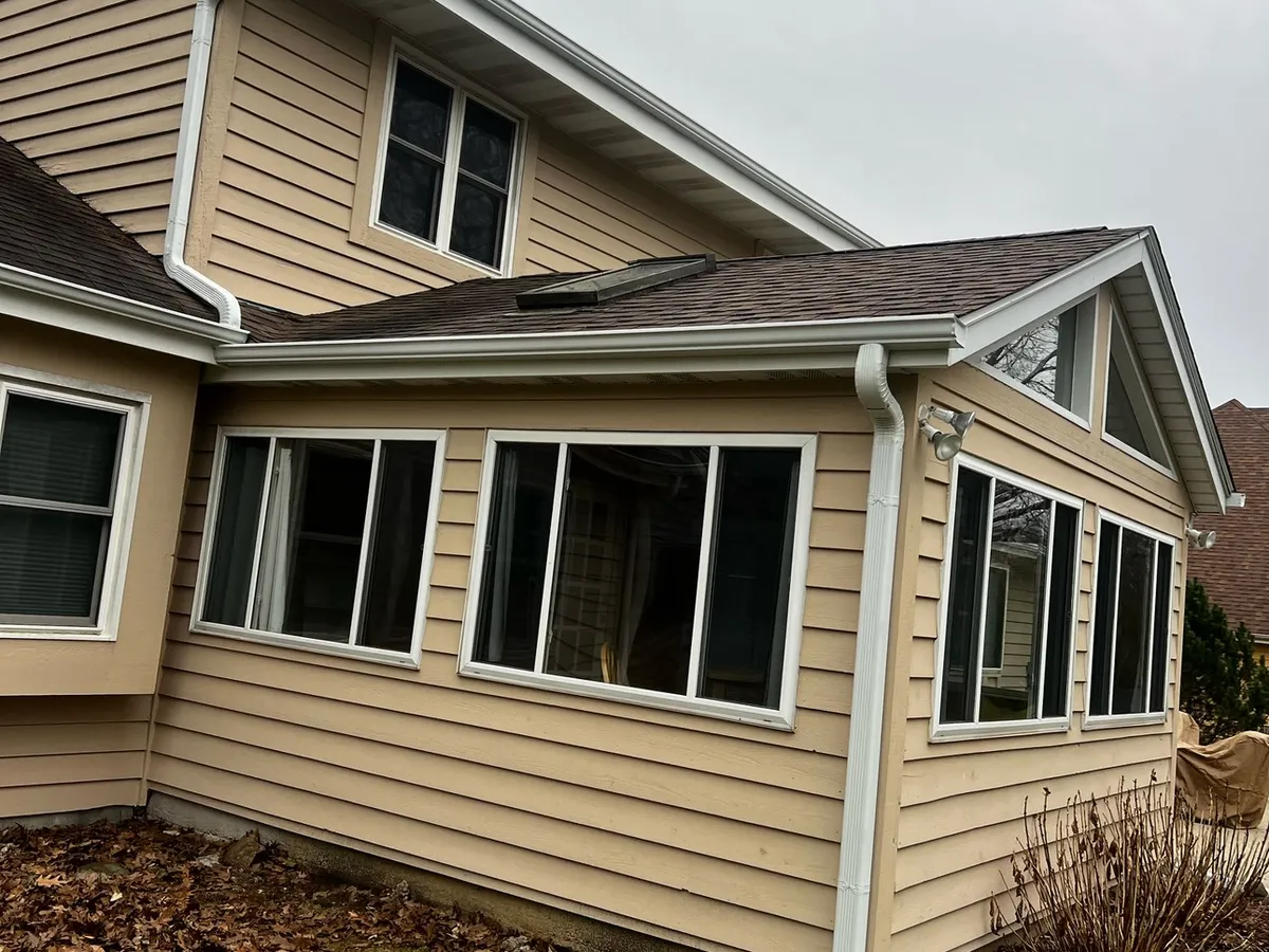 White seamless gutters installed along the rear roofline of a tan home